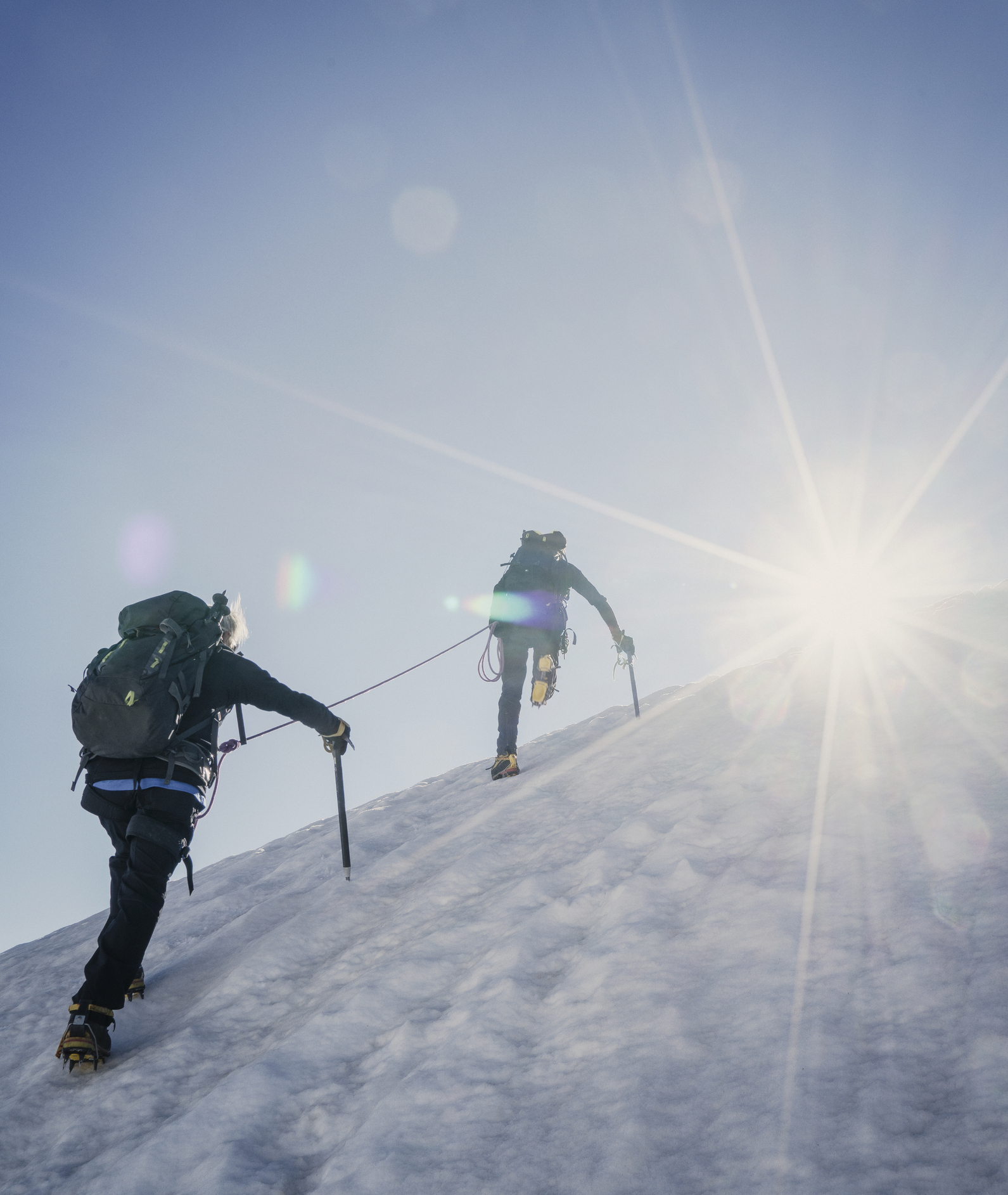 Zwei Bergsteiger am Gipfelgrat im Gegenlicht - Peak Performance